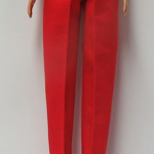 May include: Bright red doll pants with an elastic waistband. The pants have a straight leg design and are made of a textured fabric. The doll's legs and feet are visible.