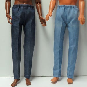 May include: Two pairs of doll pants. One pair is a dark blue denim, and the other is a light blue denim. Both have an elastic waistband and a straight leg design. The pants are displayed on two dolls.