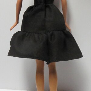 May include: A black strapless dress with a tiered skirt. The dress is made of a smooth fabric and has a simple design.