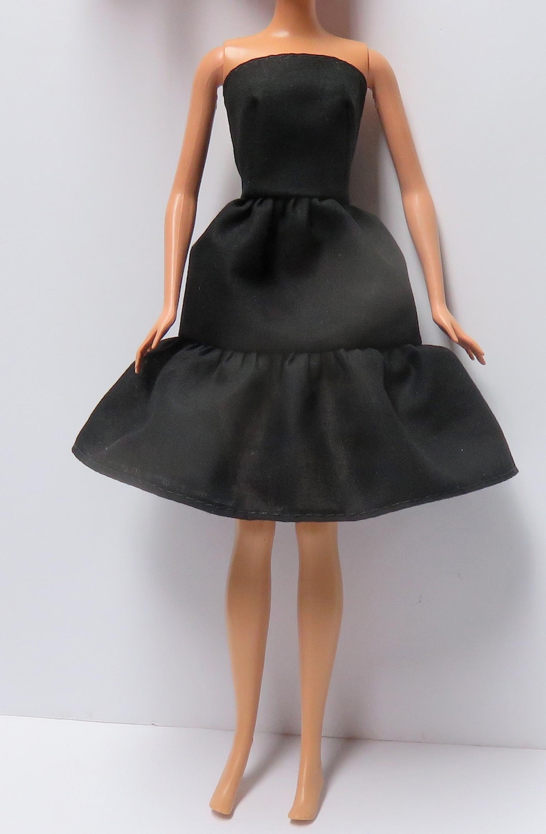 May include: A black strapless dress with a ruffled hem. The dress is made of a smooth, silky fabric.