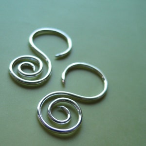 Puede incluir: Dos pendientes de plata en espiral con un diseño simple y elegante. Los pendientes están hechos de un solo alambre que se retuerce en forma de espiral.
