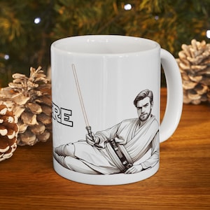 May include: White ceramic mug with a black and white illustration of a man in a robe holding a lightsaber. The text "Here" is printed on the mug.