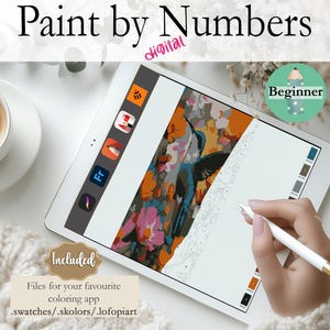 Könnte beinhalten: Ein digitales Malen-nach-Zahlen-Bild auf einem Tablet-Bildschirm. Das Bild zeigt einen Kolibri im Flug mit Blumen. Das Tablet liegt auf einer weißen Oberfläche mit einer Tasse Kaffee und einer Strickdecke.