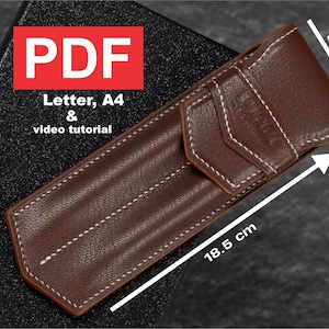 以下が含まれることがあります： 白いステッチが付いた茶色の革製のペンケース。ケースの高さは5.5cm、長さは18.5cmです。ケースには「PDF Letter, A4 & ビデオチュートリアル」とラベルが貼られています。