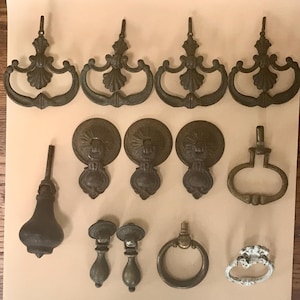 May include: A collection of antique bronze cabinet hardware, including ornate pulls, knobs, and handles. The hardware features various designs, including floral and scrollwork details, and a variety of shapes and sizes.