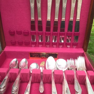 May include: A wooden box with a red velvet interior containing a set of silver flatware. The box has a label that reads "Rogers & Bro.  Revere  Silver  Original Rogers Silver  The International Silver Co."