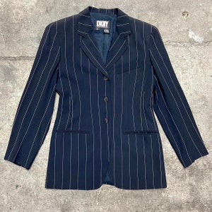 May include: A navy blue blazer with white pinstripes and a single button closure. The blazer has a DKNY label on the left side of the chest.