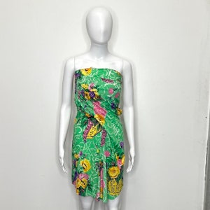 May include: A strapless green dress with a floral print featuring yellow, pink, and purple flowers. The dress has a gathered design and a fitted silhouette.
