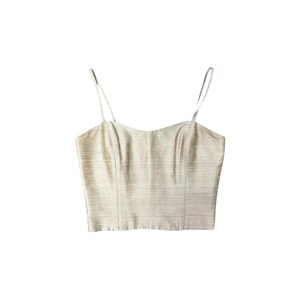 May include: A champagne-colored cropped camisole top featuring a subtle horizontal slub texture, a straight-across neckline, and two thin spaghetti straps. The garment is constructed with vertical seams along the front bodice for a structured fit.