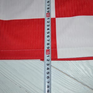 May include: A red and white checkered shirt featuring a visible measuring tape placed vertically against the fabric. The tape indicates a length measurement extending past 72 centimeters, showing the scale of the garment's patterned textile.