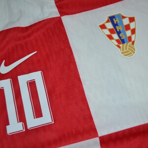 May include: A red and white checkered sports jersey featuring the number 10 in white, a white Nike swoosh logo, and the Croatian Football Federation crest with the letters HNS and a soccer ball graphic on the upper right chest area.