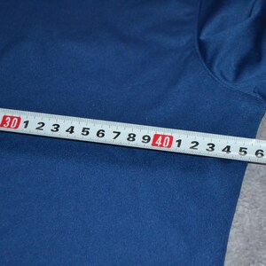 May include: A navy blue fabric is measured with a white and red ruler. The ruler shows measurements from 5 to 50 inches, equivalent to approximately 12.7 to 127 cm. The fabric is smooth.