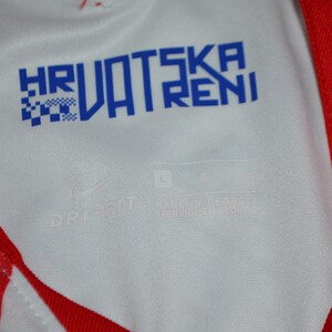 Puede incluir: Una camiseta deportiva blanca y roja con el texto azul HRVATSKA VATRENI impreso en el cuello interior. La tela incluye un logotipo de Nike y el texto DRI-FIT, con una etiqueta de talla L visible en la zona interior del cuello de la prenda.
