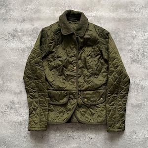 May include: Olive green quilted jacket with a corduroy collar and two front pockets. The jacket has a diamond pattern and gold-colored buttons. The brand name is visible on one of the pockets. A classic outerwear piece.