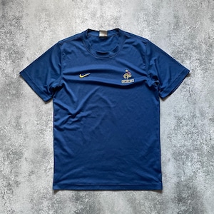 May include: A navy blue short-sleeved athletic shirt. The shirt features a yellow Nike swoosh logo on the upper left chest and a French Football Federation emblem on the right chest. The shirt is made of a lightweight, breathable material.