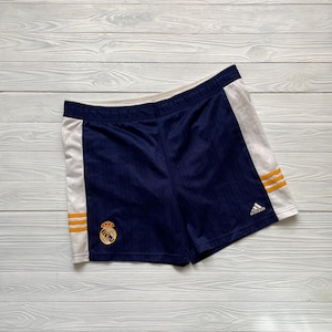 Puede incluir: Pantalones cortos deportivos azul marino con paneles laterales blancos y rayas doradas. Los pantalones cortos presentan un emblema bordado y el logotipo de Adidas. Fabricados con tejido transpirable.