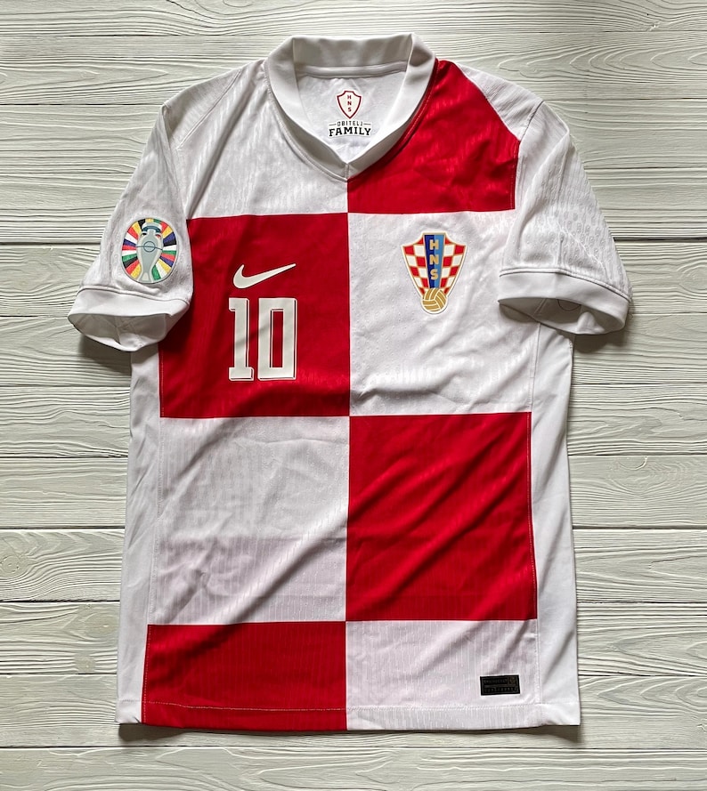 May include: A white and red checkered short-sleeve jersey featuring the number 10 in white on the front, a white Nike swoosh logo, and the Croatian Football Federation crest. The sleeve has a circular patch, and the inner collar displays HNS FAMILY.