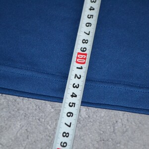 May include: Close-up of navy blue fabric with a measuring tape. The tape shows measurements in inches, with the 60-inch mark prominently displayed. The fabric appears to be a solid colour and has a smooth texture.