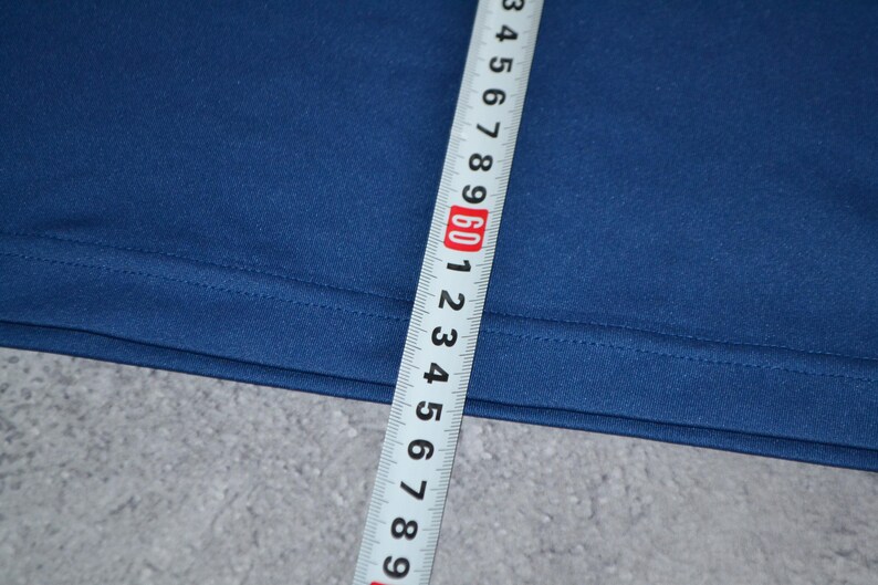 May include: Close-up of navy blue fabric with a measuring tape. The tape shows measurements in inches, with the 60-inch mark prominently displayed. The fabric appears to be a solid colour and has a smooth texture.