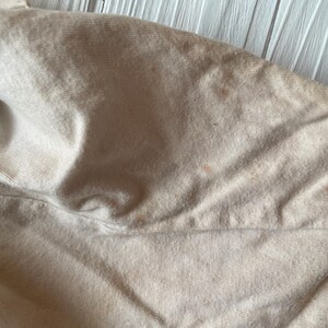 Puede incluir: Primer plano de una tela beige con pliegues y ligera decoloraci&oacute;n. La tela parece ser un material suave, posiblemente algod&oacute;n o lino, con una superficie texturizada. La imagen resalta la textura y las variaciones de color.