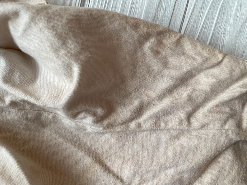 Puede incluir: Primer plano de una tela beige con pliegues y ligera decoloraci&oacute;n. La tela parece ser un material suave, posiblemente algod&oacute;n o lino, con una superficie texturizada. La imagen resalta la textura y las variaciones de color.