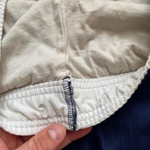 Puede incluir: Primer plano del interior de unos pantalones cortos deportivos azul marino. Los pantalones cortos tienen una cintura el&aacute;stica blanca con cord&oacute;n y un forro interior suave y claro. La tela tiene un aspecto texturizado.