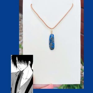 May include: A blue stone pendant necklace with a brown leather cord. The stone is oval shaped and has a speckled pattern.