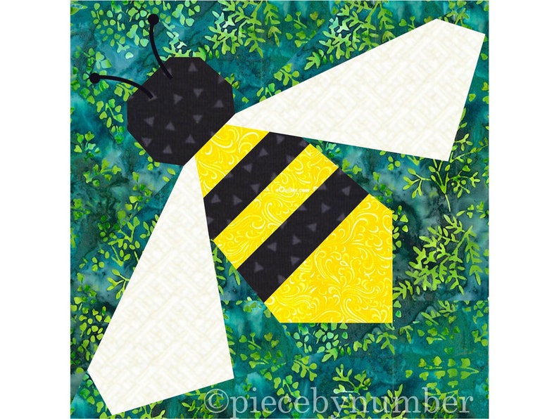 Square quilt block design of a stylized honey bee with embroidered antennae. Bee is yellow and black striped, with white wings. Background is dark green Bali batik floral.