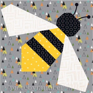 Square quilt block design of a stylized honey bee with embroidered antennae. Bee is yellow and black striped, with white wings. Background is grey with small multi-color triangles.