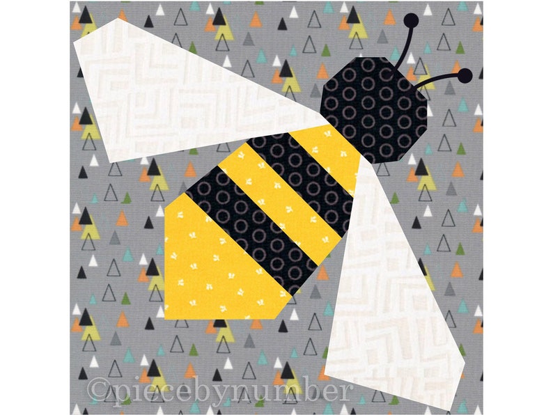 Square quilt block design of a stylized honey bee with embroidered antennae. Bee is yellow and black striped, with white wings. Background is grey with small multi-color triangles.