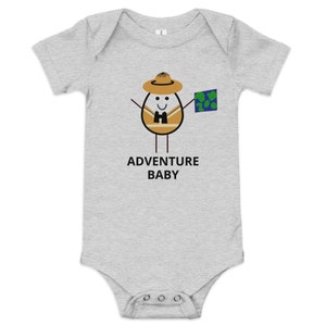 Könnte beinhalten: Ein grauer Baby-Strampler mit einem Comic-Ei, das einen Hut trägt und eine Karte hält. Der Text "ADVENTURE BABY" ist unter dem Comic gedruckt.
