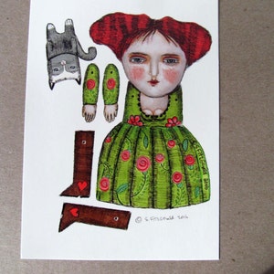 May include: A paper doll with red hair, a green dress with red roses, and brown shoes. The doll is holding a cat in its arms. The doll is part of a paper doll set. The image includes the text "S.Fitzgerald 2018".