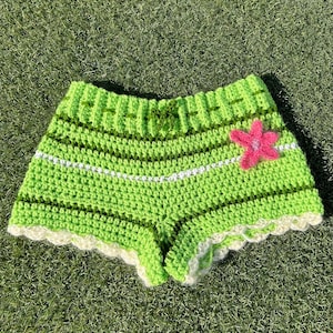 May include: Green crochet shorts with white trim and a pink flower applique.