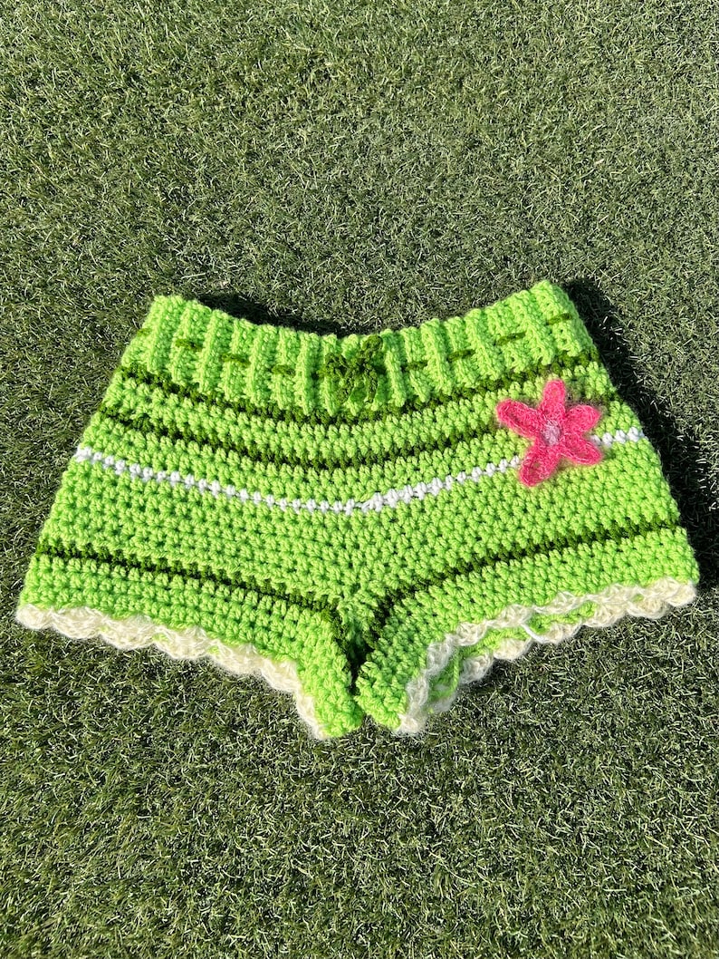 May include: Green crochet shorts with white trim and a pink flower applique.