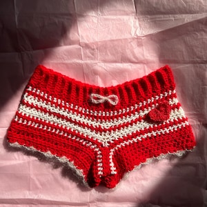 May include: Red and white crocheted shorts with a white bow and a red heart detail.