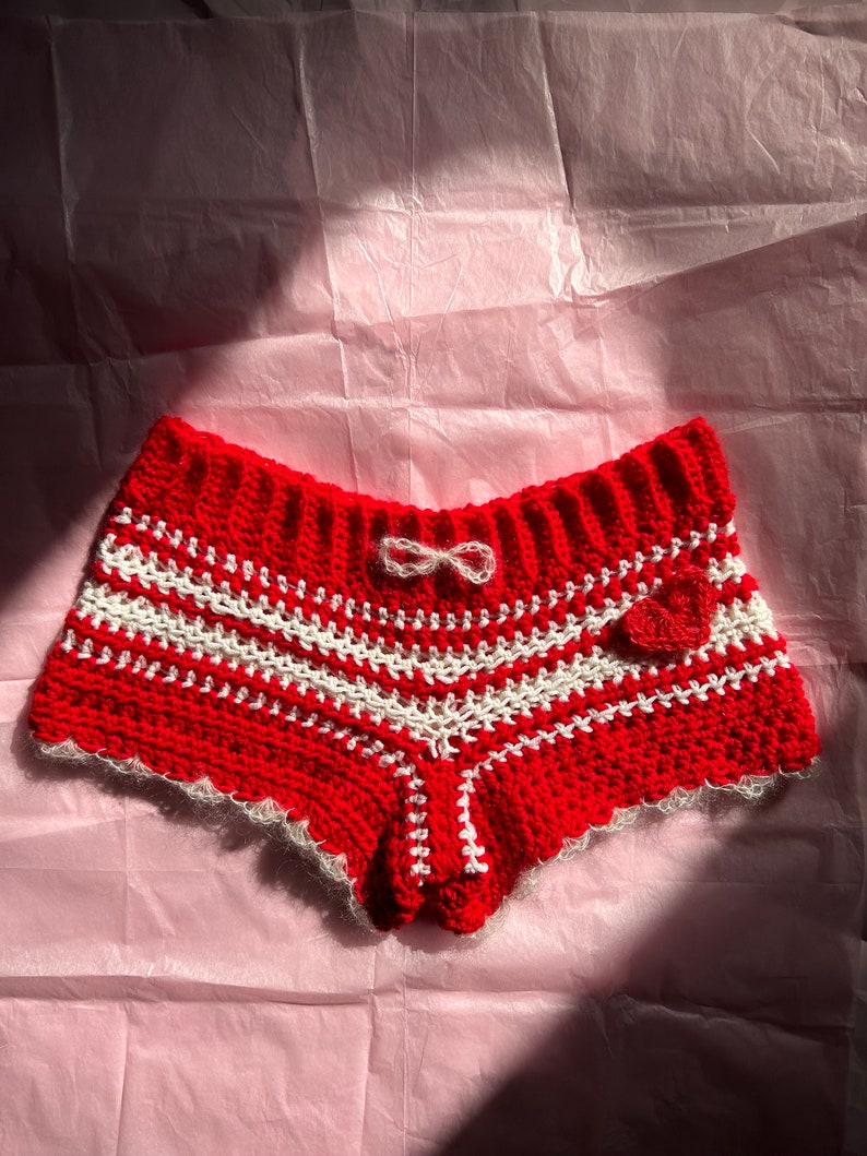 May include: Red and white crocheted shorts with a white bow and a red heart detail.