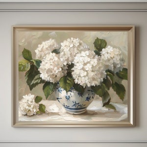 May include: A white porcelain vase with blue and white floral designs holds a bouquet of white hydrangeas. The vase is sitting on a white tablecloth.