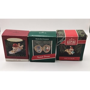 May include: Three Hallmark Christmas ornament boxes. The boxes are red, green, and black with red accents. The boxes feature images of ornaments and text including "Clip-On", "Nutshell Dreams", and "Keepsake Ornament".