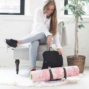 May include: A black yoga mat carrier with a pink yoga mat inside. The carrier has adjustable straps and a zippered pocket.