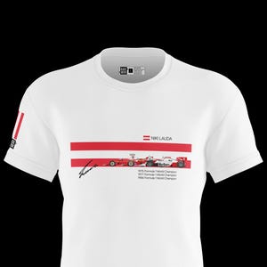 Op de afbeelding: Wit T-shirt met een ontwerp gewijd aan Niki Lauda. Het shirt bevat de Oostenrijkse vlag, rood-witte strepen, een handtekening en afbeeldingen van Formule 1-raceauto's. De tekst luidt "Niki Lauda" en vermeldt zijn Wereldkampioenschapsjaren.