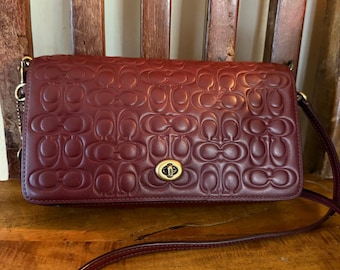 Bolso bandolera Coach Dinky 30427 de piel repujada color burdeos.