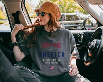 May include: A grey t-shirt with the text "the United States of America, the land of the free, home of the brave" printed on the front. A red, white, and blue heart is printed below the text.