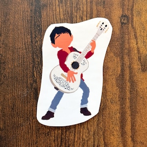 K&ouml;nnte beinhalten: Ein Aufkleber mit einer Cartoon-Illustration eines Jungen, der eine wei&szlig;e Gitarre spielt. Der Junge tr&auml;gt ein rotes Hemd, blaue Jeans und schwarze Schuhe. Die Gitarre hat dekorative Muster.