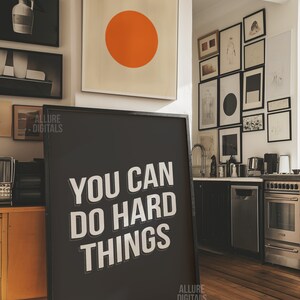 May include: A black framed motivational poster with white text that reads "You Can Do Hard Things". The poster is hanging on a wall in a modern kitchen with a stainless steel oven and dishwasher.
