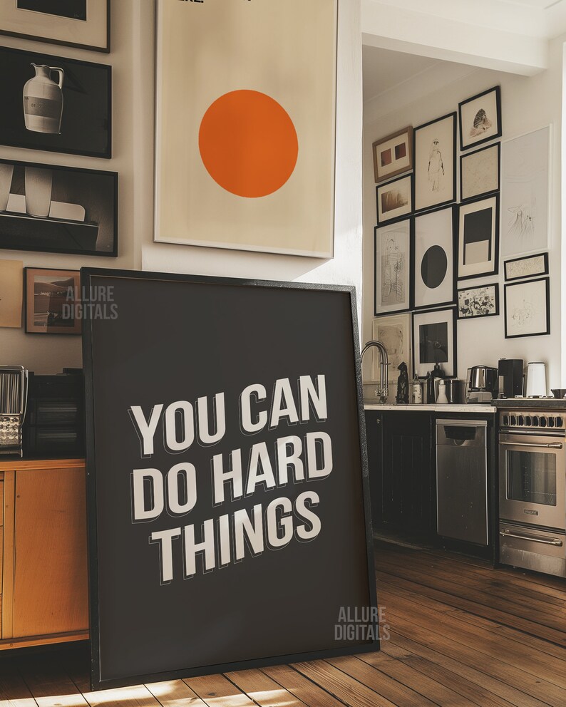 May include: A black framed motivational poster with white text that reads "You Can Do Hard Things". The poster is hanging on a wall in a modern kitchen with a stainless steel oven and dishwasher.