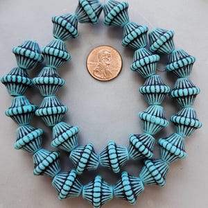 May include: Strand of turquoise and black glass beads. Each bead has a unique shape with black vertical stripes. A penny is included for size reference.