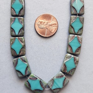 May include: Artisan-style beads with a turquoise starburst design. The beads are rectangular with a mottled green and brown finish. A penny is included for size reference. These beads are ideal for jewelry making.