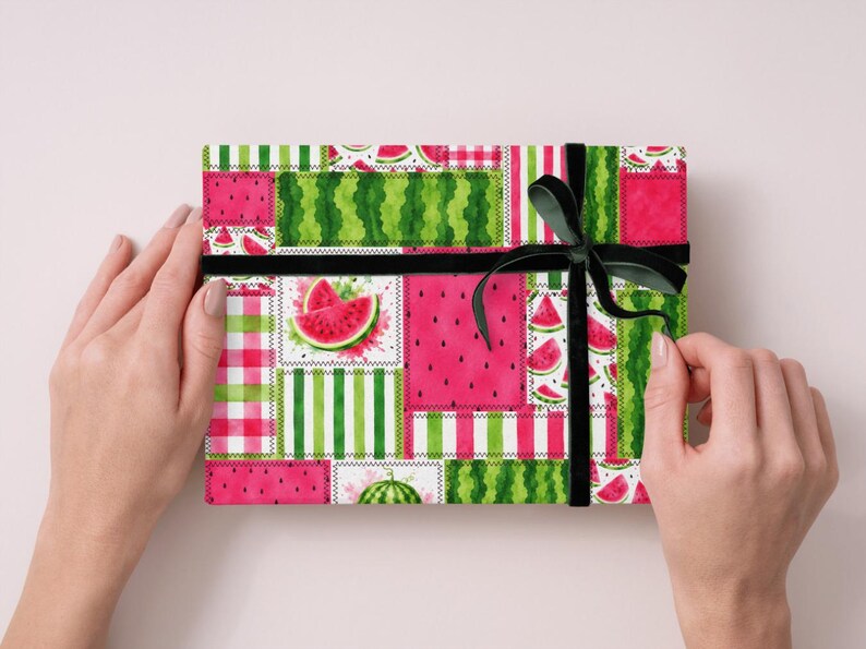 May include: A rectangular gift box wrapped in paper featuring a patchwork design of watermelon slices, seeds, and green stripes. The box is tied with a black velvet ribbon tied in a bow on the right side, showcasing a vibrant summer fruit theme.