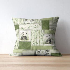 May include: Square decorative pillow with a patchwork design featuring panda bears and bamboo stalks in shades of green and white. The pillow has a stitched border and is placed on a wooden surface.