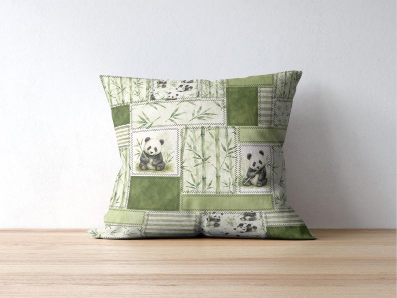 May include: Square decorative pillow with a patchwork design featuring panda bears and bamboo stalks in shades of green and white. The pillow has a stitched border and is placed on a wooden surface.